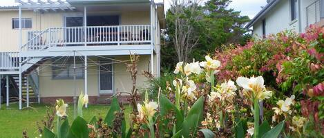 A two-story house with a balcony, surrounded by a garden with various plants and flowers.