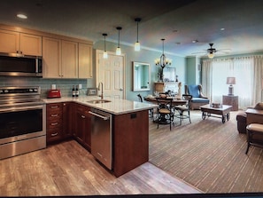 Enjoy a spacious living area with a dining table and comfortable seating, a well-equipped kitchen with a central island, and a large window with city views.