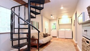 A compact living space with a spiral staircase, a sofa, a washing machine, and a kitchen area.