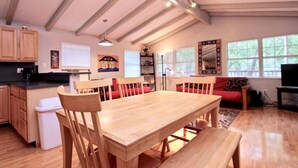 A spacious living area with a wooden dining table, red sofas, and a large window providing natural light.