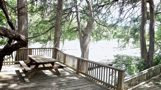 A wooden deck with a picnic table and railing overlooking a beach.