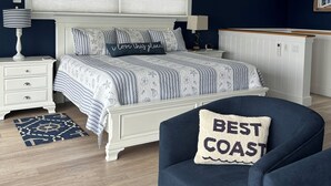 A bedroom with a bed, nightstands, a chair, a ceiling fan, and a window with blinds. - Elegant oceanfront home on Southwest Harbor minutes to trails and village center (Southwest Harbor)