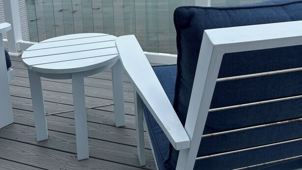 A deck with a white table and a blue chair, overlooking a calm body of water with boats and distant hills. - Elegant oceanfront home on Southwest Harbor minutes to trails and village center (Southwest Harbor)
