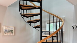 A spiral staircase with wooden steps and black metal railings in a room with wooden flooring and a white wall. - Elegant oceanfront home on Southwest Harbor minutes to trails and village center (Southwest Harbor)