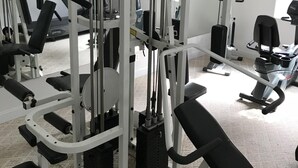 A gym with various exercise machines, a bench, and a mirror.