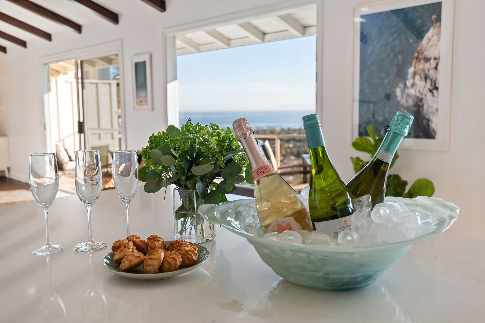 A table with champagne bottles, glasses, and a plate of food in a room with a view.
