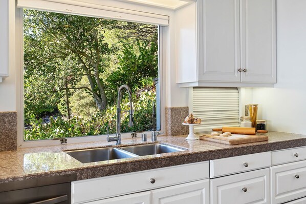 A kitchen with a large window, granite countertops, white cabinets, and a view of greenery outside. - Amazing Ocean, Island, and City Views From Contemporary Home! (Santa Barbara)