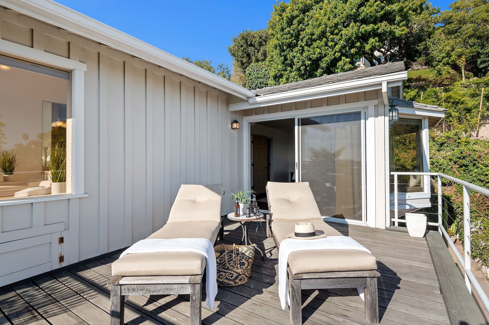 A deck with two lounge chairs, a small table with a hat, and a sliding glass door leading to a covered area.