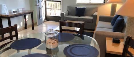 A dining area with a glass table, four chairs, and a central glass container.