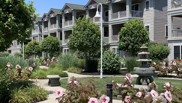 A multi-story residential building with balconies and a landscaped garden with pink flowers and a stone lantern.