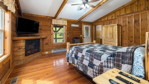 Quarto de cabana de madeira com cama, televisão, lareira e ventoinha no teto.
