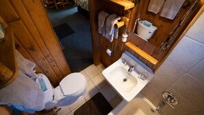 A wooden cabin bathroom with a toilet, sink, and wooden shelves.