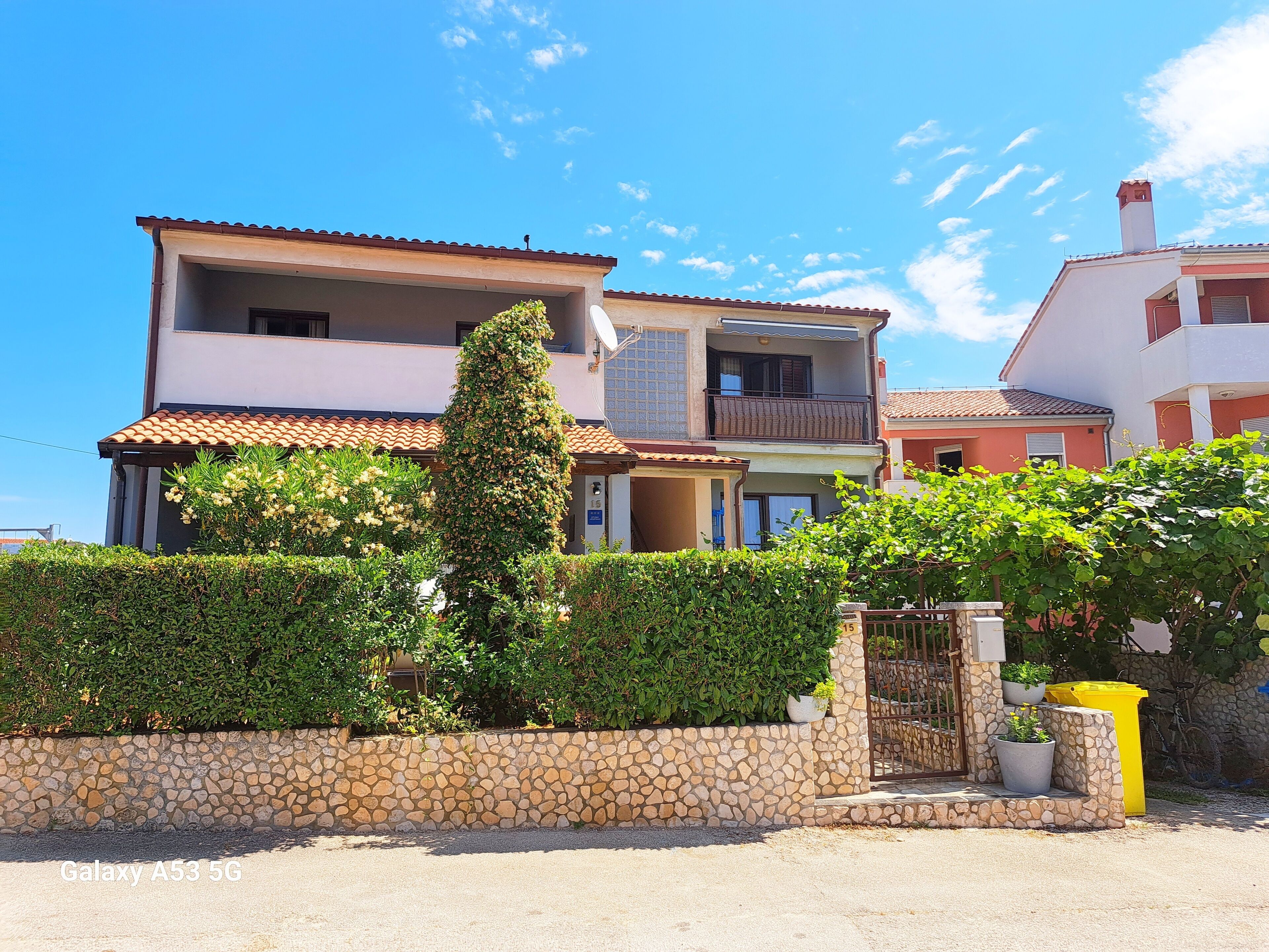 A two-story house with a stone wall, a balcony, and a garden.