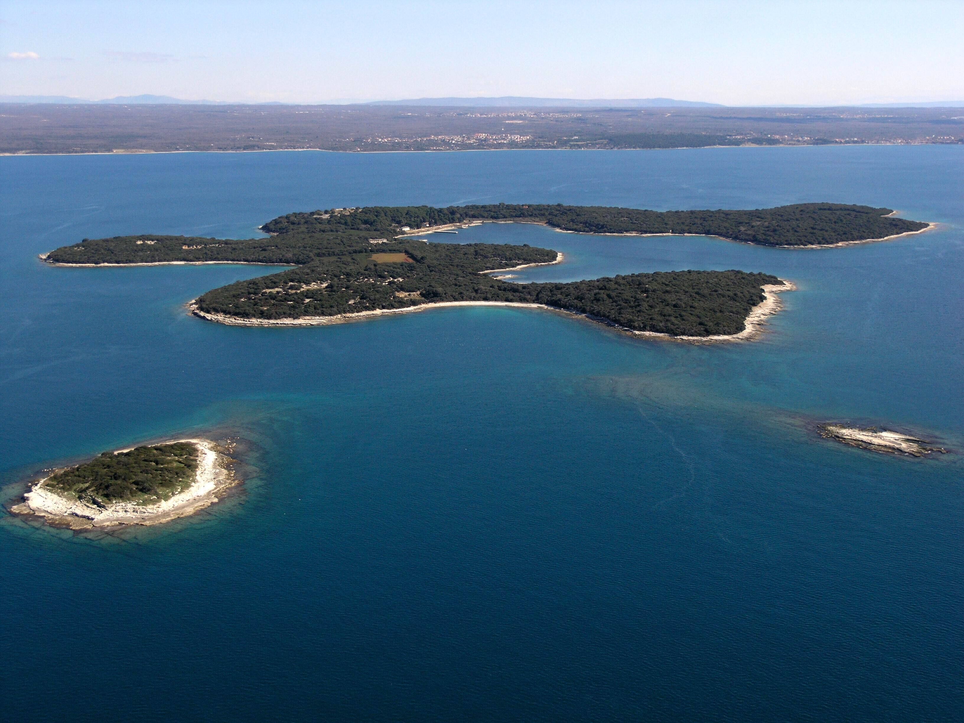 Eine Vogelperspektive zeigt eine Inselgruppe mit klarem, blauem Wasser und dichtem Grünland.