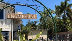 Une pancarte indiquant « GNOMEVILLE » au-dessus d’une porte, avec une foule de personnes et des palmiers en arrière-plan.