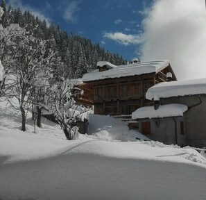 Un chalet de madera con techo nevado, rodeado de árboles cubiertos de nieve y un cielo despejado.