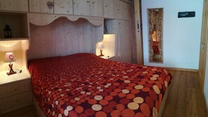 Ein Schlafzimmer mit einem Holzkopfteil, einer rot gepunkteten Tagesdecke und einem Nachttisch mit einer Lampe.