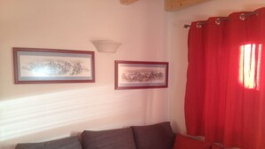 Ein Wohnzimmer mit einem braunen Sofa, roten Vorhängen und zwei gerahmten Bildern an der Wand.