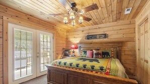 A wooden cabin bedroom with a bed, a ceiling fan, and a sign on the wall.