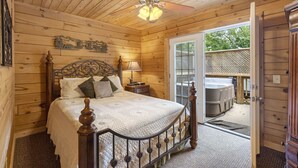 A wooden cabin bedroom with a bed, a nightstand, a lamp, and a ceiling fan. - Premium Rustic Cabin Perfect Getaway, Private Hot Tub,Piano, Near Shows & Big Cedar, Jacuzzi Tub! (Ridgedale)