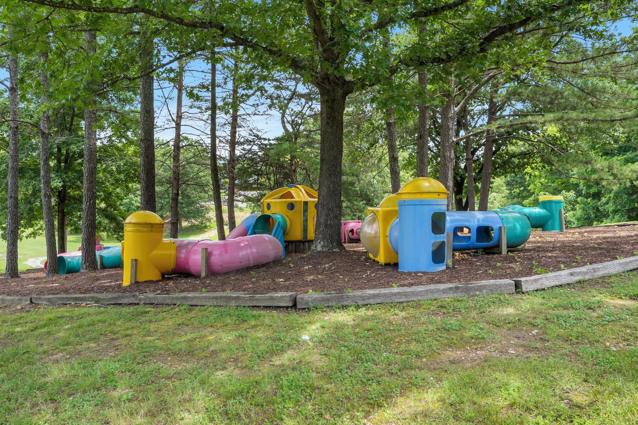 Un parque infantil con toboganes coloridos y estructuras de juego rodeado de árboles.