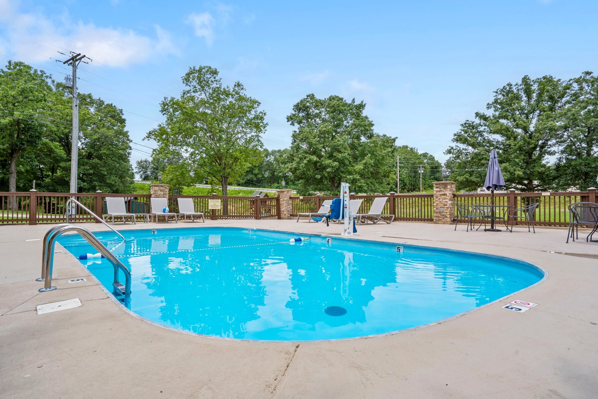 A swimming pool with a diving board, lounge chairs, and a stone pillar.