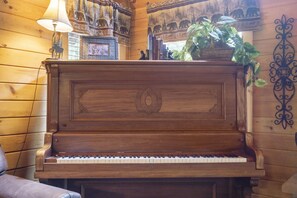 Un piano en bois orné de sculptures décoratives, entouré de livres, d’une lampe et d’une plante.