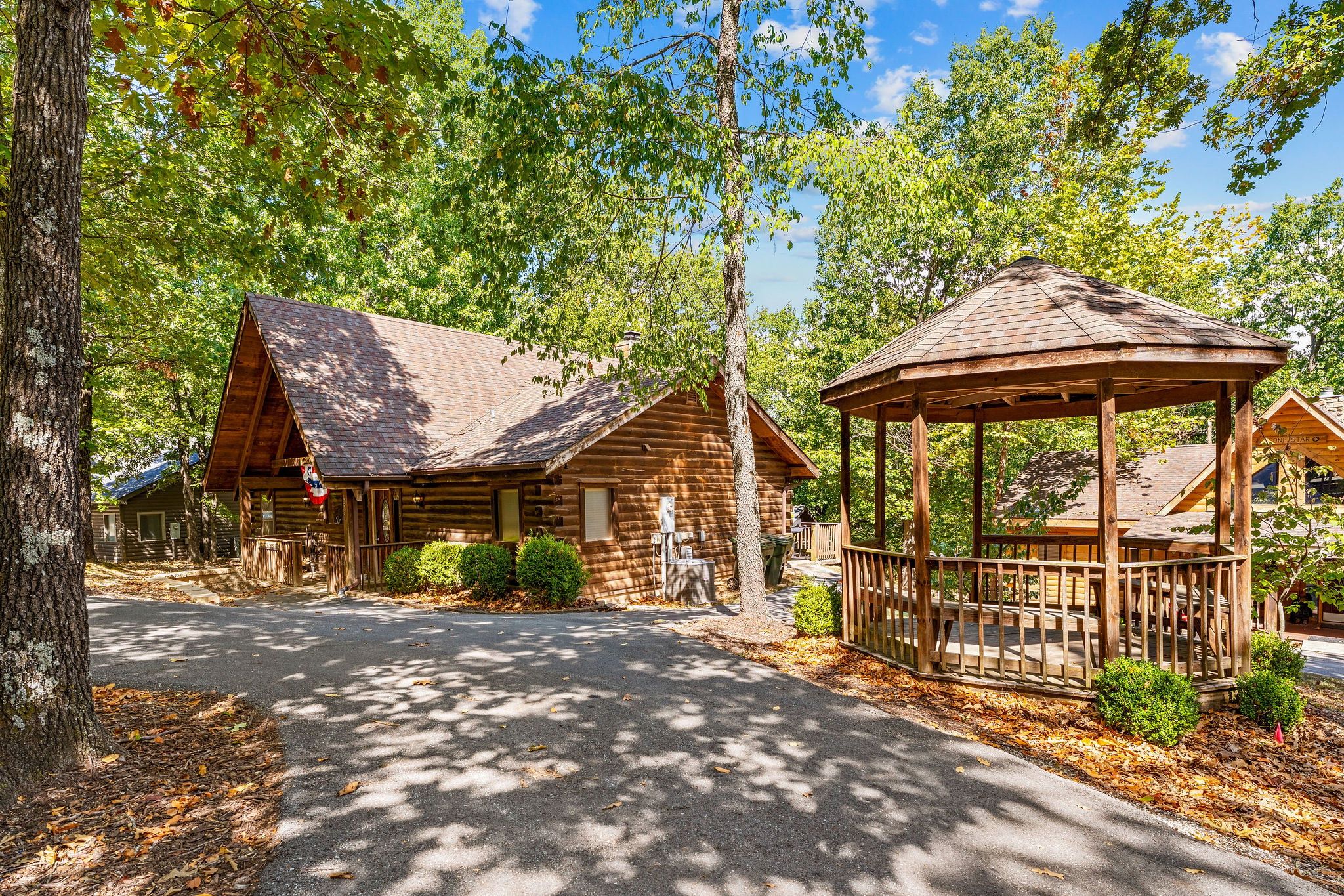A rustic lodge with a gazebo and log cabins, surrounded by trees.
