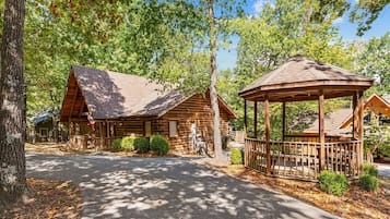A rustic lodge with a gazebo and log cabins, surrounded by trees.