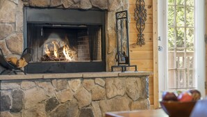 A stone fireplace with a fire, a wooden door with a window, and a decorative metal piece on the wall. - Premium Rustic Cabin Perfect Getaway, Private Hot Tub,Piano, Near Shows & Big Cedar, Jacuzzi Tub! (Ridgedale)