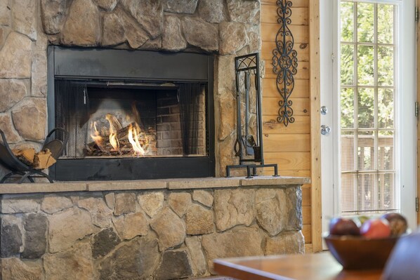Une cheminée en pierre avec un feu, une porte en bois dotée d’une fenêtre et un élément décoratif en métal fixé au mur.