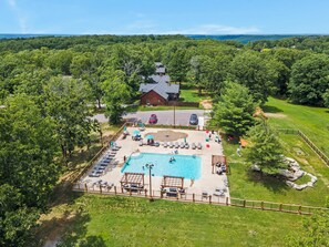 An aerial view of a resort with a swimming pool, lounge chairs, and a rustic building.