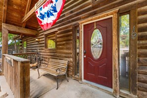 A wooden cabin with a red door, a bench outside, and a flag hanging above.