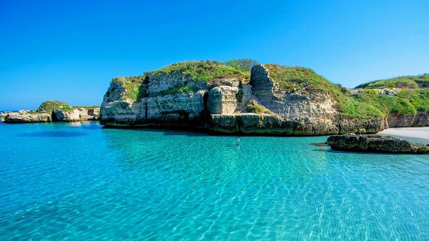 A coastal scene with clear turquoise waters, rocky formations, and a sandy beach. - Seafront apartment. 3 double beds and 3 bathrooms (Gallipoli)
