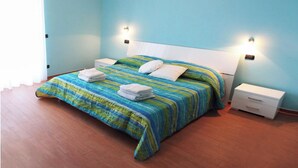 A neatly made bed with a striped bedspread and two pillows, a bedside table with a lamp, and a window with curtains. - Seafront apartment. 3 double beds and 3 bathrooms (Gallipoli)