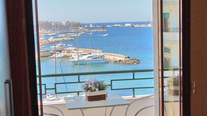 A balcony with a view of the sea and boats, a small table with chairs, and a bed with a folded blanket. - Seafront apartment. 3 double beds and 3 bathrooms (Gallipoli)