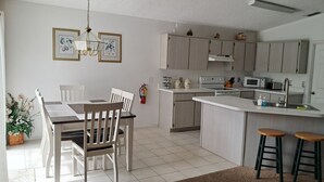 A modern kitchen with a dining area, white cabinetry, and a central island. - 'Lakeside Haven'  Fantastic South Facing Pool, Spa and Stunning Lakeside Views. (Kissimmee)
