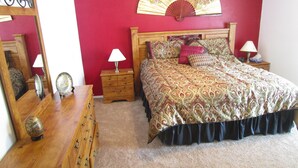 A bedroom with a wooden bed, a nightstand with a lamp, a dresser, and a mirror. - 'Lakeside Haven'  Fantastic South Facing Pool, Spa and Stunning Lakeside Views. (Kissimmee)
