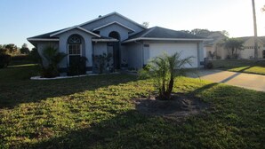 A single-story house with a sloped roof, a front porch, and a small front yard with a palm tree. - 'Lakeside Haven'  Fantastic South Facing Pool, Spa and Stunning Lakeside Views. (Kissimmee)