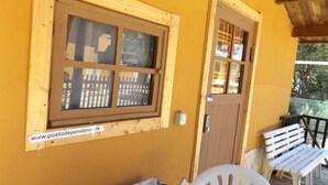 Ventana de madera con vistas a una valla, una puerta y una silla de plástico blanca en el exterior.