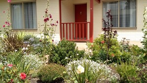 A house with a red front door, a balcony, and a garden with various plants and flowers. - Ten-on-French Barossa getaway (Angaston)