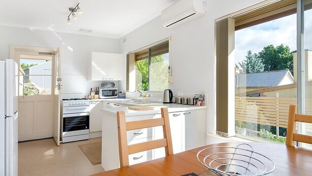 A modern kitchen with white cabinetry, a built-in oven, microwave, and sink. There is a dining area with a wooden table and chairs. - Ten-on-French Barossa getaway (Angaston)