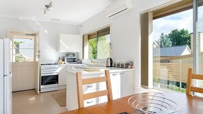 A modern kitchen with white cabinetry, a built-in oven, microwave, and sink. There is a dining area with a wooden table and chairs. - Ten-on-French Barossa getaway (Angaston)