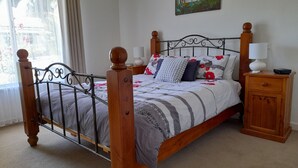 A bedroom with a wooden bed frame, a bedside table, a nightstand, a painting on the wall, and a window with curtains. - Ten-on-French Barossa getaway (Angaston)