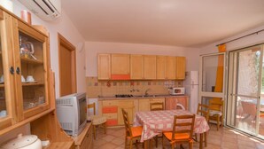 A compact kitchen with wooden cabinets, a microwave, a stove, and a dining table with chairs. - Borghetto Tio Pepe - Trilo 6 Mandarin (Mattinata)