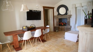 A dining area with a wooden table and white chairs, a flat-screen TV mounted on the wall, and a stone fireplace with a mirror above it. - Villa Falgheri with swimming pool for 6 people - Itria Valley (Ostuni)