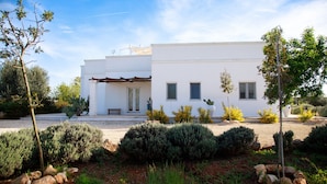 A modern white building with a covered porch, surrounded by landscaped gardens and cacti. - Villa Falgheri with swimming pool for 6 people - Itria Valley (Ostuni)