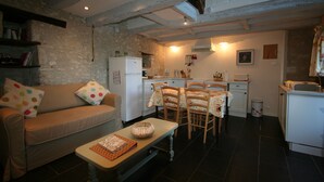 A cozy living room with a sofa, a coffee table, and a dining area with chairs and a table. There is a kitchen area with a refrigerator, stove, and sink. - Walnut Lodge, charming holiday Gite in central rural France (Pleumartin)