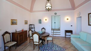 A dining area with a round table, chairs, a chandelier, a sofa, and a staircase leading to an upper floor. - ATRANI "CASA ROSSA" AMALFI COAST WITH SEA VIEW (ATRANI)