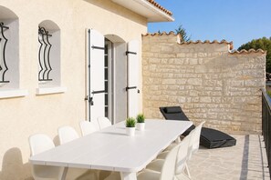 Une terrasse avec une table et des chaises blanches, un mur en pierre et une chaise noire.